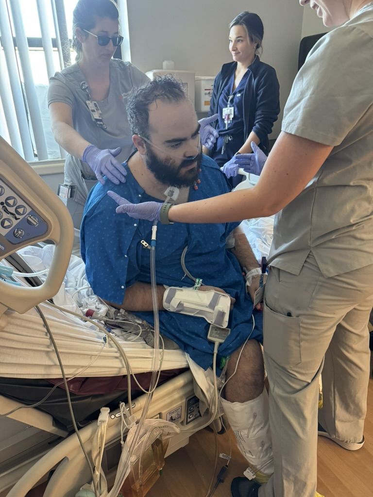 A care team supports Michael as he sits at the edge of his hospital bed.